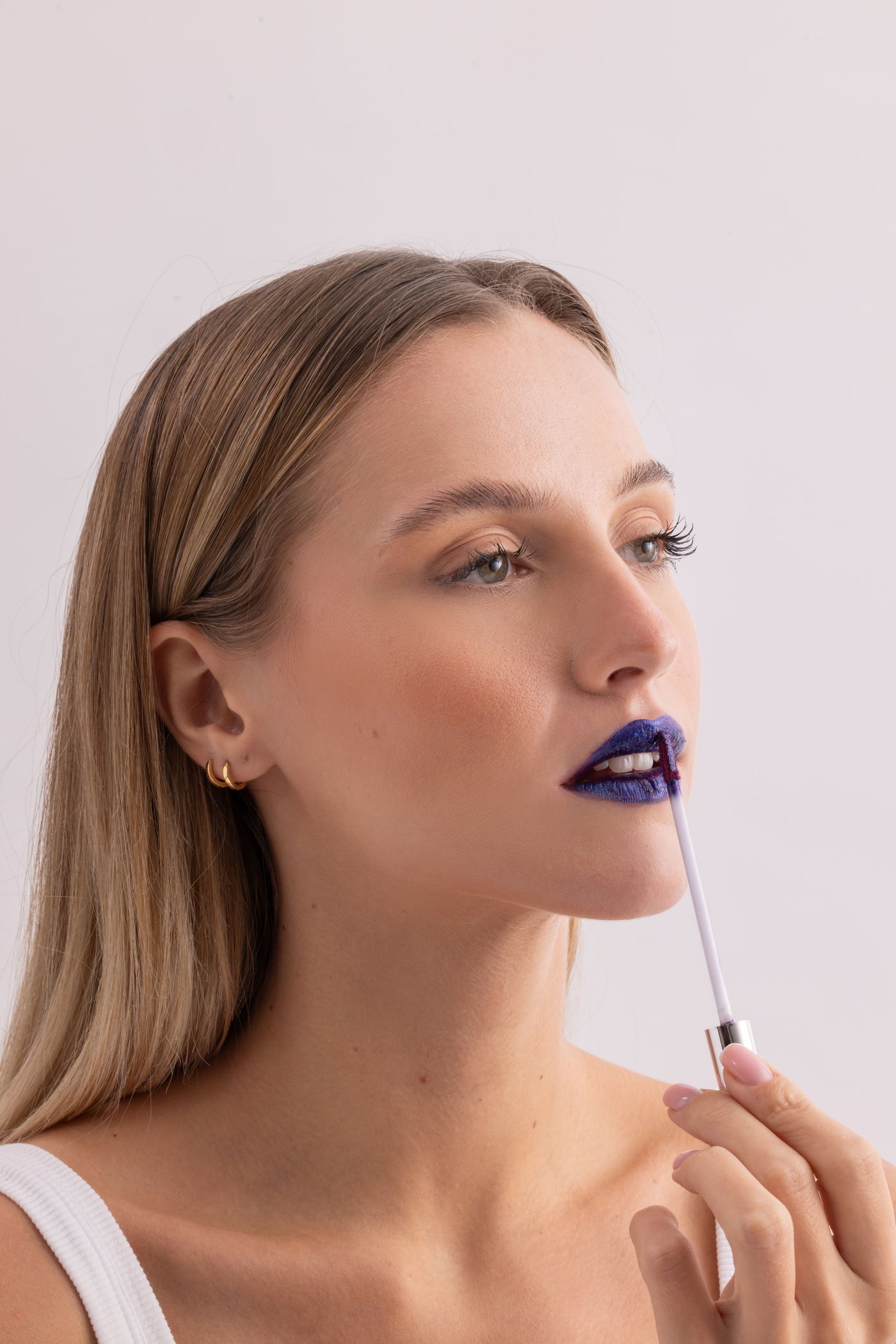 Model applying bold blue Stay-On Lip Stain on white background